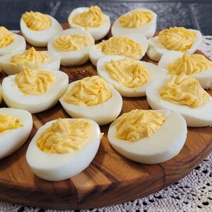 May include: A wooden platter filled with deviled eggs. The eggs are white with a yellow yolk filling. The platter is on a white crocheted tablecloth.