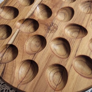 May include: A round wooden tray with 18 circular indentations, perfect for serving appetizers or snacks. The tray has a natural wood finish and a floral design in the center.