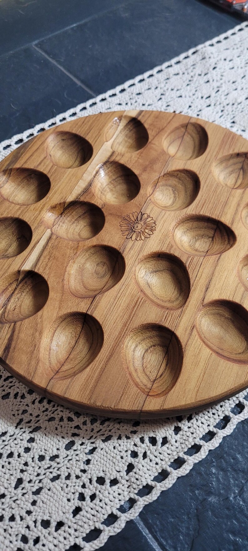 May include: A round wooden tray with 18 circular indentations, perfect for serving appetizers or snacks. The tray has a natural wood finish and a floral design in the center.