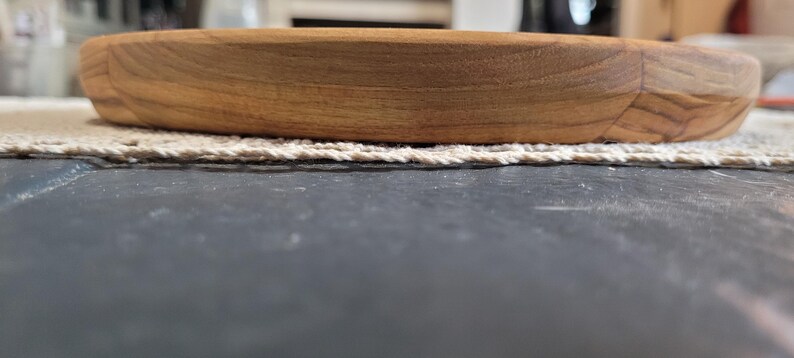 May include: A round wooden serving tray with a natural wood finish. The tray has a slightly raised edge and is made of solid wood.