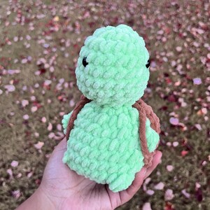 May include: A handmade, light green crochet turtle with a brown shell. The turtle has black eyes and is made of a soft, textured yarn. The turtle is a plush toy, perfect for children or as a decorative item.