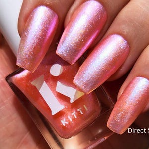 May include: A hand displays long, iridescent pink nails. A coral-coloured nail polish bottle with the brand name "Kitti" is held. The text "Direct Sun" is visible. The nails have a shimmering finish.