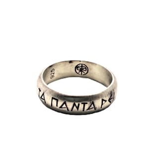 May include: A silver ring with the inscription "TA PANTA REI" in Greek letters. The ring has a brushed finish and a small emblem and the number "925" on the top. The ring is a piece of jewelry.