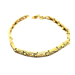 Könnte beinhalten: Ein goldfarbenes Armband mit einem sich wiederholenden geometrischen Muster. Das Armband besteht aus verbundenen rechteckigen Segmenten, die jeweils ein griechisches Schlüsseldesign aufweisen. Der Verschluss ist oben sichtbar.