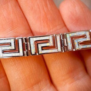 May include: Silver bracelet with a Greek key pattern and white opal inlays. The bracelet is made up of rectangular links, each showing the geometric design. The opal inlays have a slight iridescent quality, adding a touch of colour.