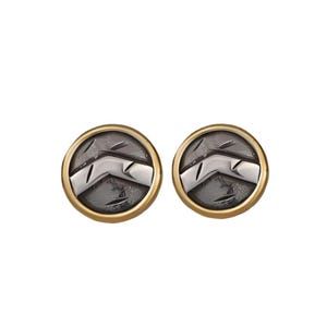 May include: A pair of round stud earrings. Each earring has a silver and black design within a gold-coloured border. The design appears to be a stylized shield or emblem.