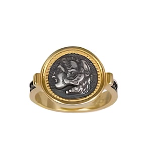 Könnte beinhalten: Ein goldfarbener Ring mit einem dunklen Cameo, das eine klassische Figur darstellt. Der Ring hat ein breites Band und eine kreisförmige Fassung mit schwarzem Hintergrund. Das Cameo ist in Grau- und Weißtönen gehalten und in einen goldenen Rahmen gefasst.