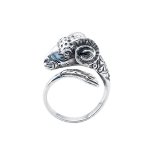 May include: A silver-colored ring featuring a detailed ram's head design. The ram's head is positioned at the top of the ring, with the curved band wrapping around. The ring has an open design, allowing for some size adjustment. The ram's head has intricate detailing.
