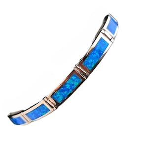 May include: A silver bracelet with rectangular blue opal inlays. The bracelet has a hinged design and is set against a white background. The blue opal has a vibrant, speckled appearance.