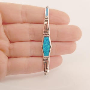 May include: A silver bracelet with a blue opal stone set in a geometric design. The bracelet is made of sterling silver and features a delicate chain.