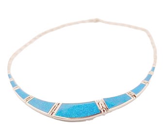 May include: A silver-toned necklace with a curved design. The necklace features sections of bright blue, possibly turquoise, with silver accents. The necklace is on a white background.