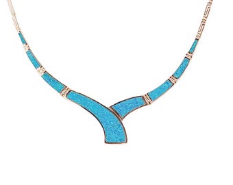 May include: A silver-toned necklace with a turquoise inlay design. The necklace features a curved, Y-shaped pendant with a mosaic-like pattern of bright blue stones. The chain is delicate and has small rectangular links.