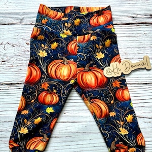 May include: Dark blue leggings with a repeating pattern of orange pumpkins, yellow and orange leaves, and swirling vines. The leggings have a high waist and fitted cuffs. The text "@Hi Donna!" is visible.