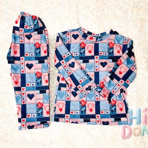 May include: A blue and pink long-sleeved shirt and matching pants with a patchwork design featuring hearts. The fabric has a quilted texture.