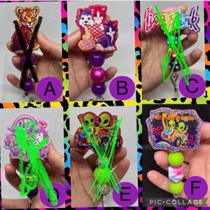 May include: A collection of six retractable badge holders with various designs. The designs include a leopard, cats, aliens, and a retro-themed alien design. Each holder has a beaded accent and a clip.