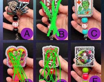 May include: A collection of six horror-themed badge reels featuring acrylic character designs including Freddy, a blood donor graphic, and Pennywise. Each reel is accented with colorful, textured beads and a retractable cord mechanism for ID cards.