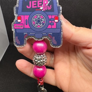 May include: A badge reel featuring a navy blue and pink Jeep design with the text "Jeep Girl." The reel has pink and silver beads and a clear plastic clip.
