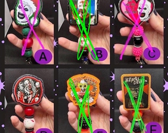 May include: Six badge reels featuring horror-themed designs labeled A through F. Each reel has a decorative topper with character graphics, including clowns and movie icons, attached to a retractable cord with colorful, textured plastic beads.
