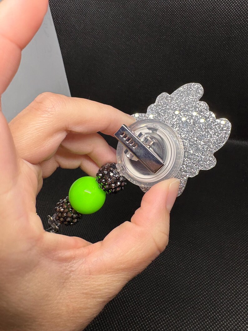 May include: A silver glitter charm with a clear plastic backing and a silver clip. The charm is attached to a beaded chain with a green bead.