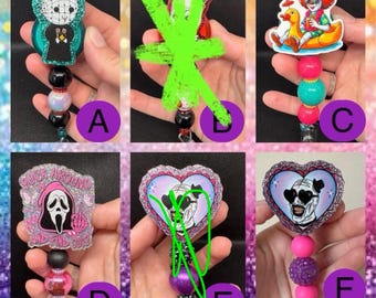 May include: A collection of six retractable badge holders with various horror-themed designs. The designs include characters like Pinhead, Pennywise, and the Ghostface mask. Each badge holder has a unique bead and charm design.