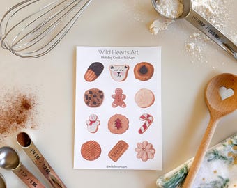 May include: A sheet of stickers featuring illustrations of various holiday cookies, including gingerbread, sugar cookies, and candy canes. The stickers are arranged in a grid pattern on a white background. The text "Wild Hearts Art" and "Holiday Cookie Stickers" is printed at the top of the sheet. The text "@wildhearts.art" is printed at the bottom of the sheet.