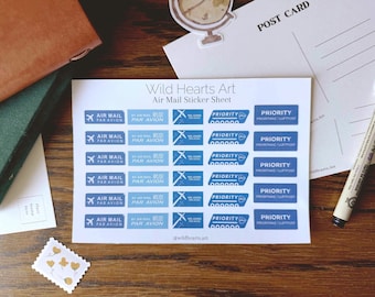 May include: A sheet of blue and white air mail stickers with the text "Air Mail" and "Priority". The sheet also includes the text "Wild Hearts Art". A postcard, pen, and other stationery items are also visible.