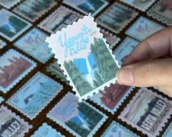 May include: A collection of vintage-style postage stamps featuring various national park scenes. One stamp is held up, showcasing a waterfall and the text "Yosemite Falls 1890". Other stamps depict landscapes and text like "Lassen Volcanic National Park".