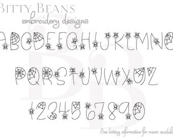 May include: A black and white alphabet and number set with a Halloween theme. The letters and numbers are outlined in black, with spiderwebs and spiders incorporated into the design. The text "Bitty Beans embroidery designs" is at the top.