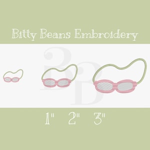May include: An embroidered design featuring three pairs of pink and white swimming goggles with a green strap. The sizes are labeled as 1", 2", and 3" in white text. The words "Bitty Beans Embroidery" are at the top.