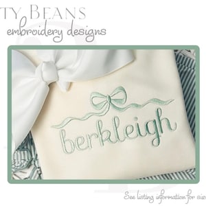 Op de afbeelding: Crèmekleurige stof met de naam "berkleigh" geborduurd in een zachtgroen script, geaccentueerd door een bijpassend strikdesign. De tekst "Bitty Beans embroidery designs" staat bovenaan.