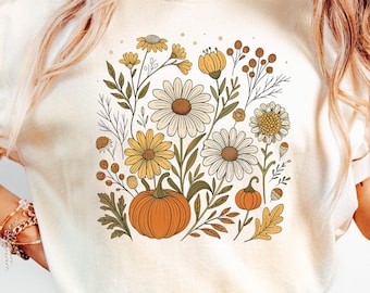 May include: Ivory-colored t-shirt featuring a floral design with daisies, yellow flowers, and pumpkins. The graphic has a vintage aesthetic with a fall theme. The shirt is a relaxed fit.