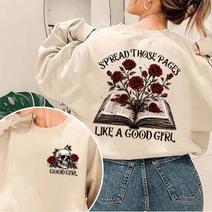 May include: Cream-colored sweatshirt with a graphic of an open book with red roses and the text "SPREAD THOSE PAGES LIKE A GOOD GIRL." A smaller image on the front features a skull and roses with the text "GOOD GIRL."