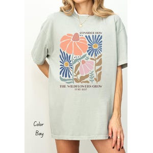 K&ouml;nnte beinhalten: Ein hellgr&uuml;nes T-Shirt mit einem Blumendesign und dem Text "Consider How The Wildflowers Grow Luke 12:27".
