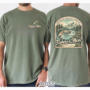 Könnte beinhalten: Moosgrünes T-Shirt mit einer kleinen Fischgrafik und dem Text "Fishers of Men" auf der Vorderseite. Die Rückseite zeigt eine größere Grafik eines Fisches, der aus einem Fluss mit Bergen und Bäumen springt, sowie den Text "Follow Me and I Will Make You" und "Fishers of Men".