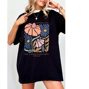K&ouml;nnte beinhalten: Schwarzes Oversize-T-Shirt mit einem floralen Motiv und dem Text "Consider how the wildflowers grow Luke 12:27".