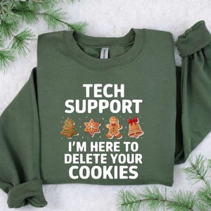 Może przedstawiać: Ciemnozielona bluza z napisem "TECH SUPPORT" i frazą "I'M HERE TO DELETE YOUR COOKIES." Projekt zawiera ilustracje choinki, gwiazdy, piernikowego ludzika i dzwonka.