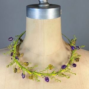 May include: A green wire necklace with purple and brown glass beads, resembling a vine with leaves and berries.