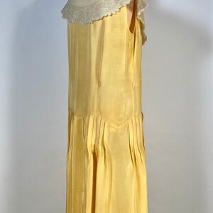 May include: A sleeveless yellow silk dress with a white lace collar. The dress has a pleated skirt and a fitted bodice.