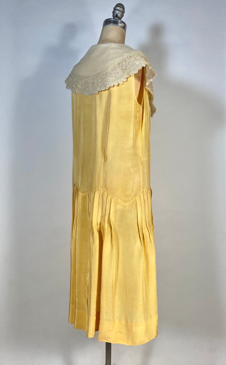 May include: A sleeveless yellow silk dress with a white lace collar. The dress has a pleated skirt and a fitted bodice.