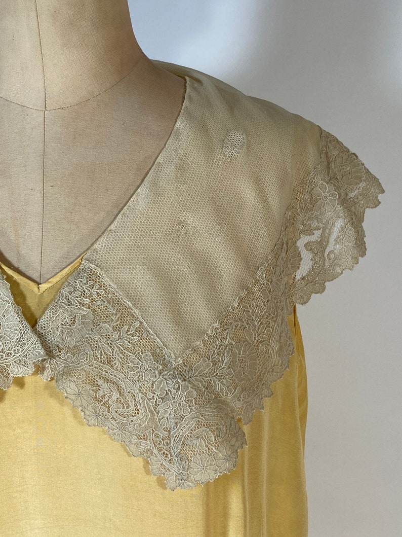 May include: A yellow vintage dress with a large, white lace collar. The collar is trimmed with delicate floral lace.