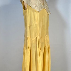 May include: A sleeveless yellow silk dress with a white lace collar. The dress has a V-neckline and a pleated skirt.