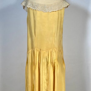 May include: A sleeveless yellow silk dress with a white lace collar. The dress has a pleated skirt and a fitted bodice.
