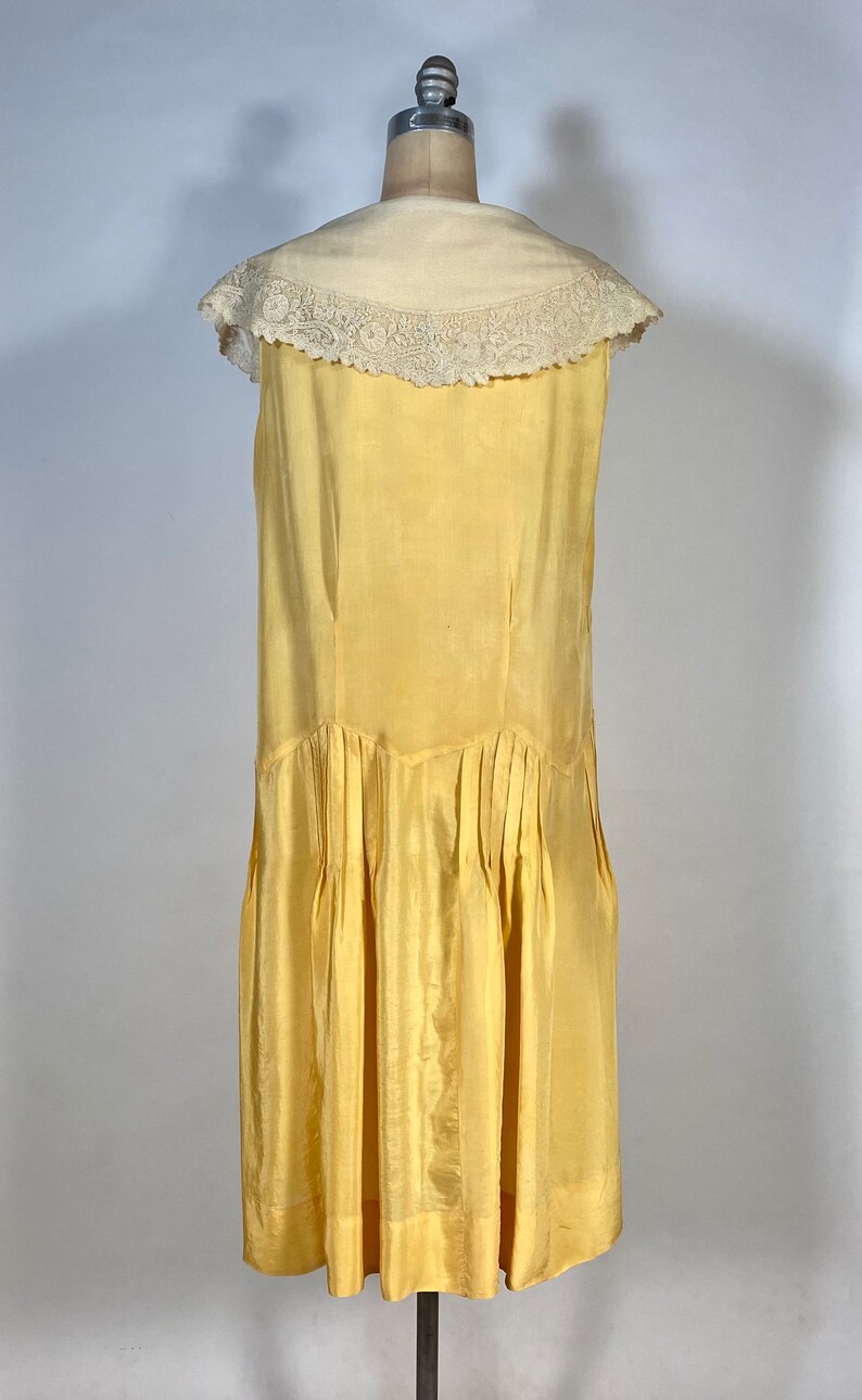 May include: A sleeveless yellow silk dress with a white lace collar. The dress has a pleated skirt and a fitted bodice.