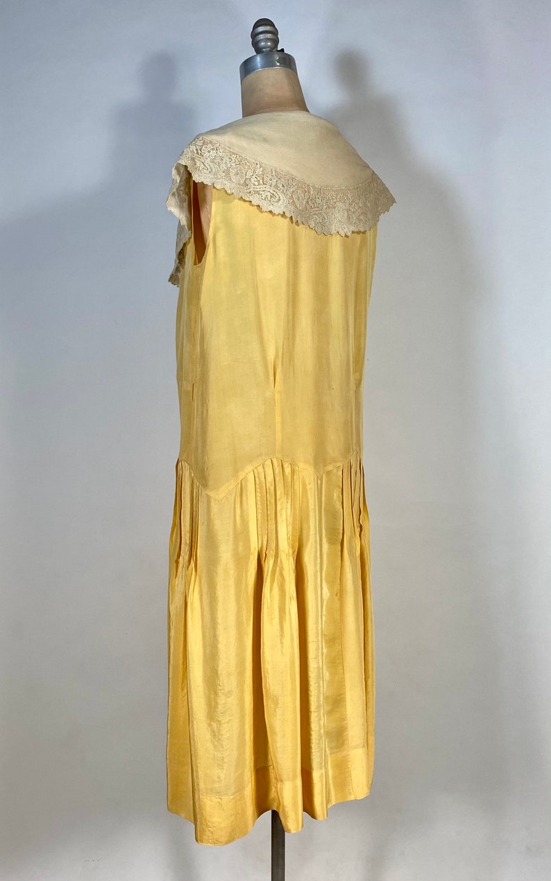 May include: A sleeveless yellow silk dress with a white lace collar. The dress has a pleated skirt and a fitted bodice.