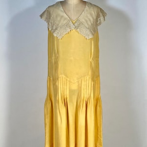 May include: A sleeveless yellow dress with a white lace collar. The dress has a pleated skirt and a fitted bodice.
