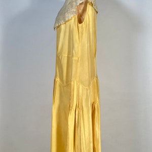 May include: A yellow sleeveless dress with a white lace collar. The dress has a pleated skirt and is made of a silky fabric.