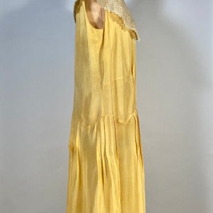 May include: A yellow sleeveless dress with a lace collar. The dress has a pleated skirt and is on a mannequin.