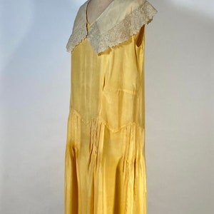 May include: A yellow silk dress with a white lace collar. The dress has a pleated skirt and a sleeveless design.