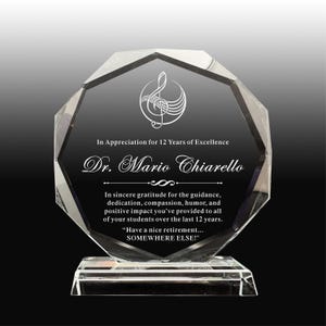 Puede incluir: Un premio de cristal claro y facetado con un diseño de nota musical y texto. La inscripción dice "En agradecimiento por 12 años de excelencia" y está dedicado al Dr. Mario Chiarello. Incluye un mensaje de jubilación.