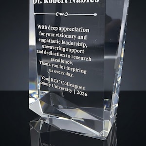 May include: A clear, faceted glass award trophy featuring an engraved inscription that reads: Dr. Robert Nables, With deep appreciation for your visionary and empathetic leadership, unwavering support and dedication to research excellence. Thank you for inspiring us every day. Your RGC Colleagues Emory University | 2026.